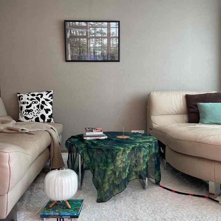 Natural tone living room with beige sofas and white rug, featuring a green forest patterned tablecloth and a nature poster for a cozy atmosphere