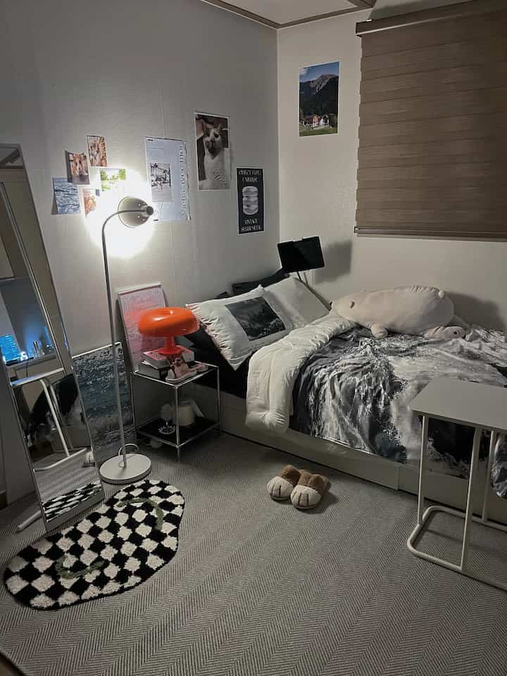 Monotone studio bedroom with gray floor and white walls, featuring a modern bed, side table, cat posters, and mood lighting creating cozy atmosphere