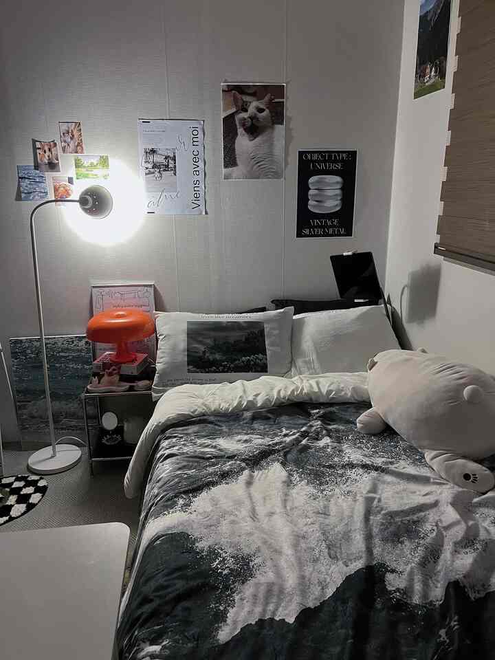 モノトーン調の寝室、波の柄のブランケットとオレンジ色の照明、ポスターが配置された雰囲気のある空間