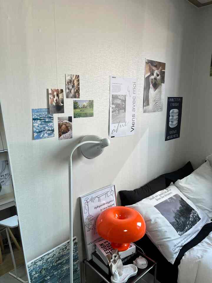 A cozy bedroom with white walls and bed, decorated with pet photos and a bright orange lamp