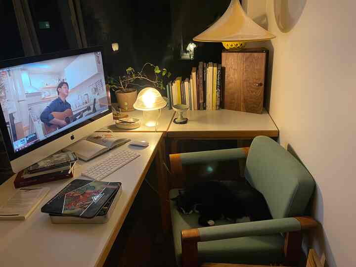 Cozy home office with warm lighting and natural tones; desk setup beside an armchair where a cat sleeps peacefully