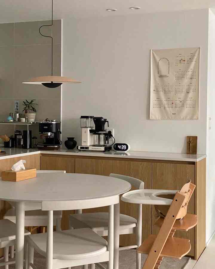 White and wood tone kitchen and dining area featuring a round table and baby chair in a simple modern interior