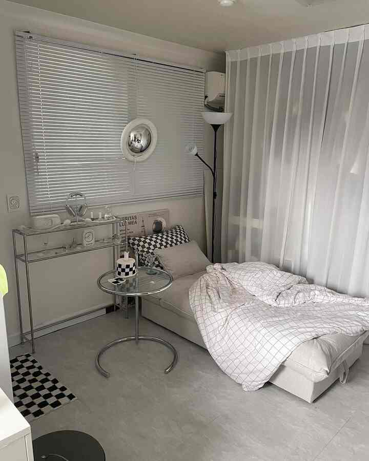 A white and beige toned living room featuring a sofa bed, metal side table, and floor lamp creating a modern atmosphere