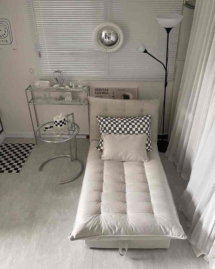 オートミール色のナチュラルなリビング、中央にソファベッドとクロームのサイドテーブル、ブラインドとフロアランプが配置されたシンプルでモダンなインテリア