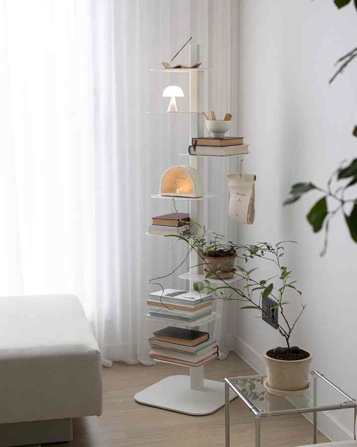 White-toned studio apartment featuring a central bookshelf and plants, presenting a minimal and clean space