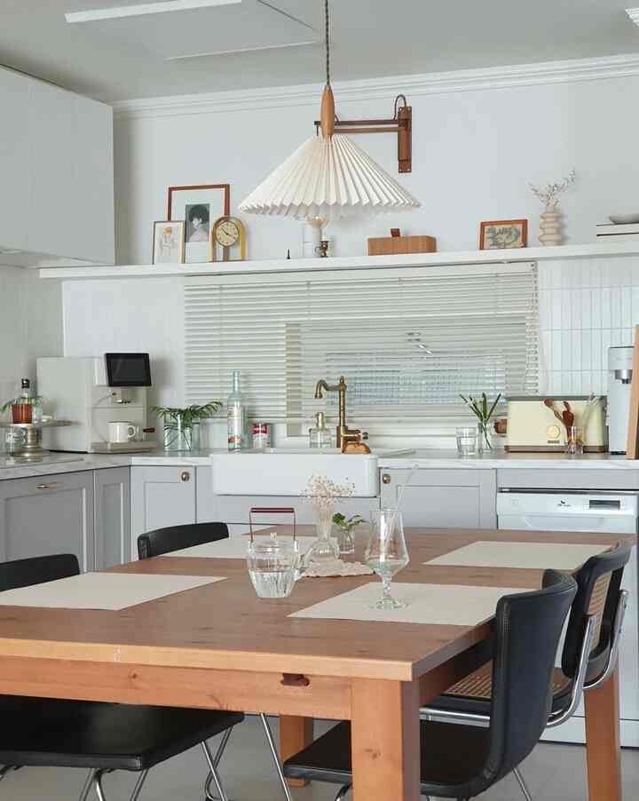A modern kitchen with white and wood tones, featuring a wooden dining table and pendant light in a simple setting