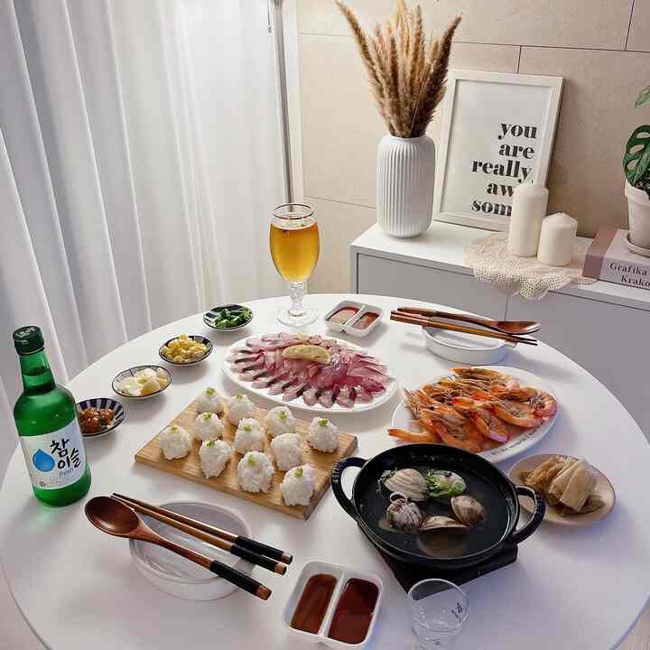 White-toned dining room featuring a round dining table with sashimi, shrimp, rice balls, and drinks arranged for a natural and cozy drinking atmosphere