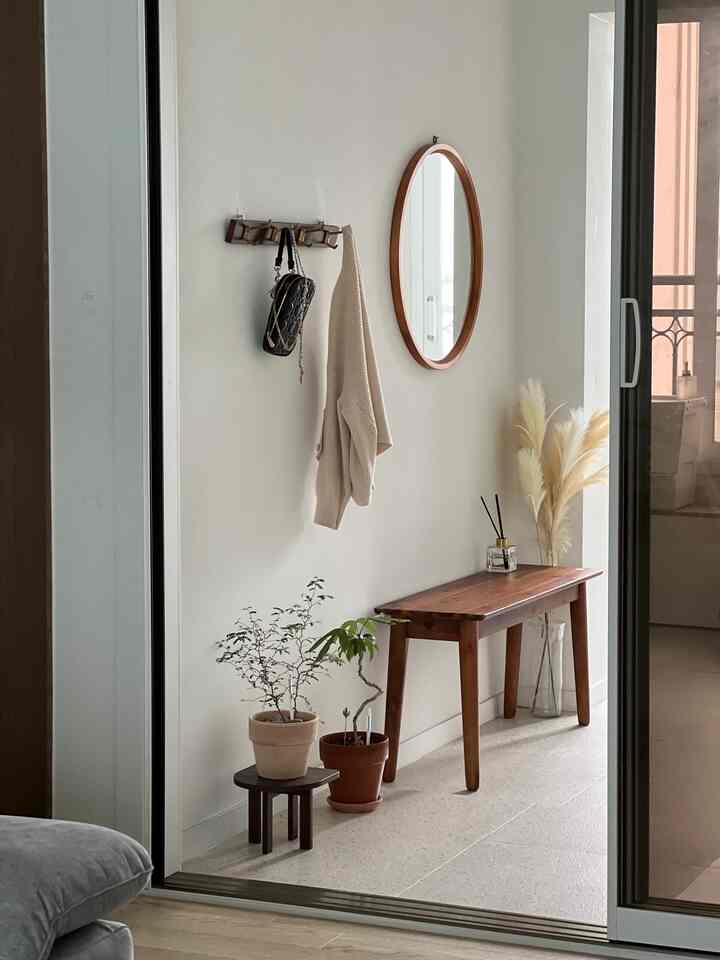 Bright and calm white-walled entrance featuring a wood tone bench, plants, and diffuser creating a natural ambiance