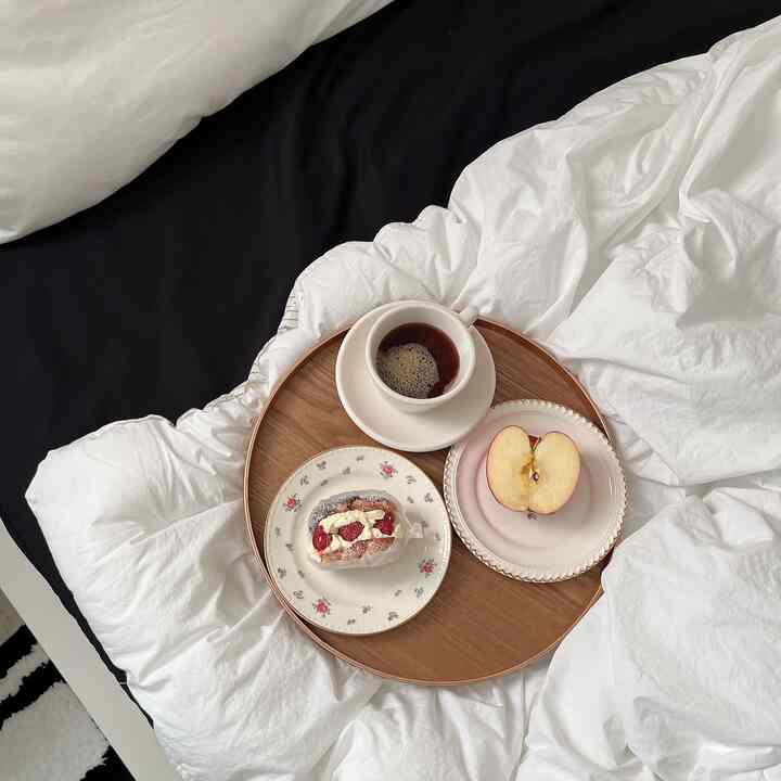 白い寝具と丸い木製トレイにコーヒーとデザート、リンゴが置かれたナチュラルスタイルの寝室インテリア