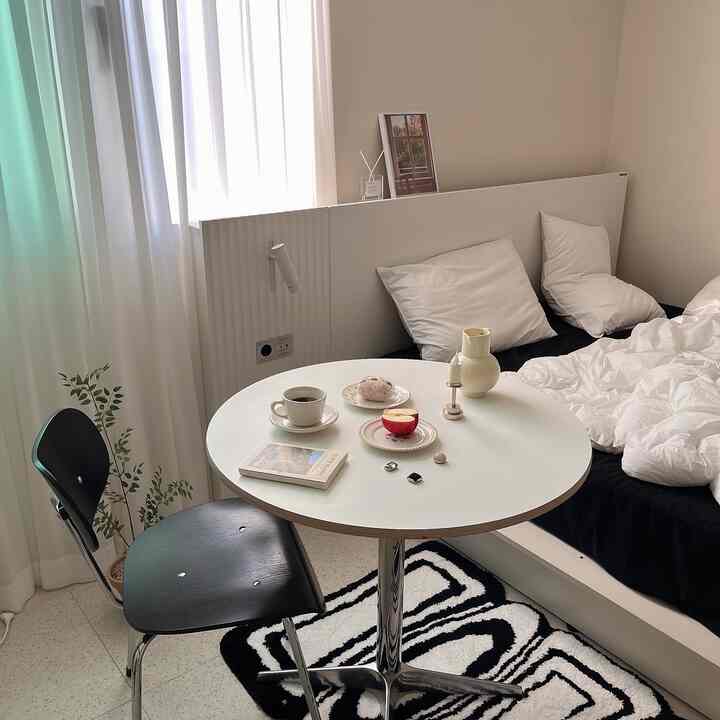 White and black toned bedroom featuring a round nightstand and black chair in a compact natural space
