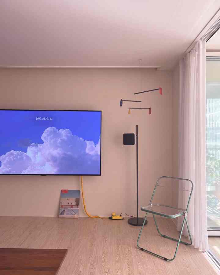 Beige-toned living room featuring wall-mounted TV, transparent acrylic chair, and mobile light fixture with a modern natural feel