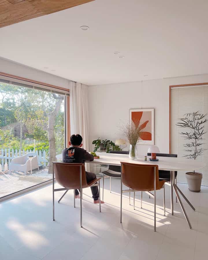 White and brown toned dining room featuring large windows with curtains, dining table and chairs creating a clean natural space