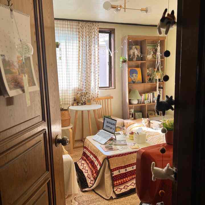 Wood tone and natural color small living room featuring a kotatsu table, bookshelf, and a cat lounging by the window with a cozy vintage feel