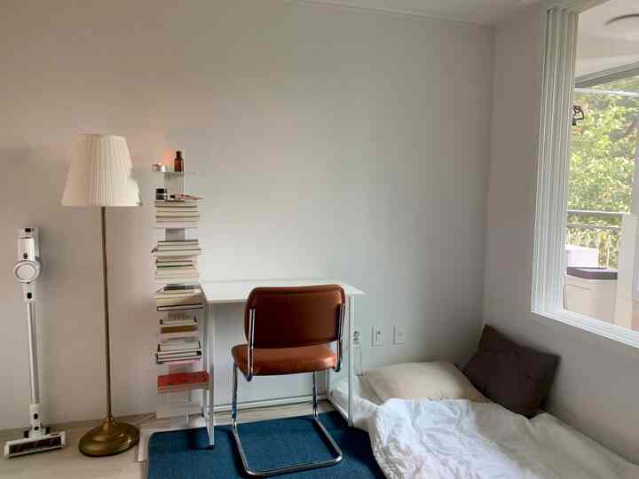 A small room in white and brown tones featuring a desk, chair, and floor bed with a simple atmosphere