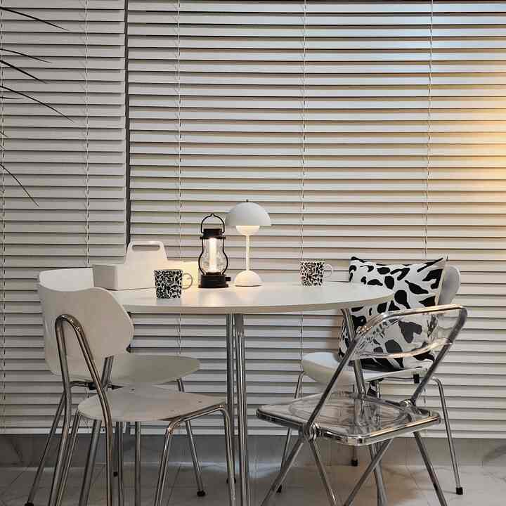 White-tone veranda space featuring round table with chairs, blinds in background, creating a cozy modern home bar setup