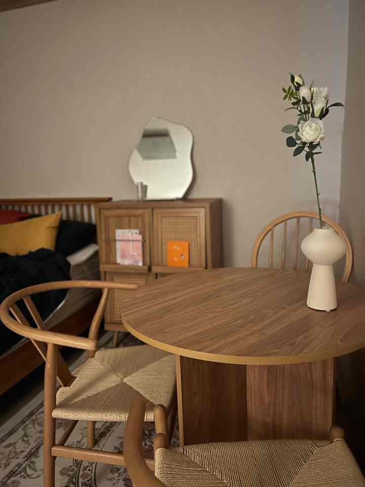 ベージュの壁と木目調の家具が調和するダイニングルーム、木製のテーブルと椅子、花瓶が配置された落ち着いた雰囲気のインテリア