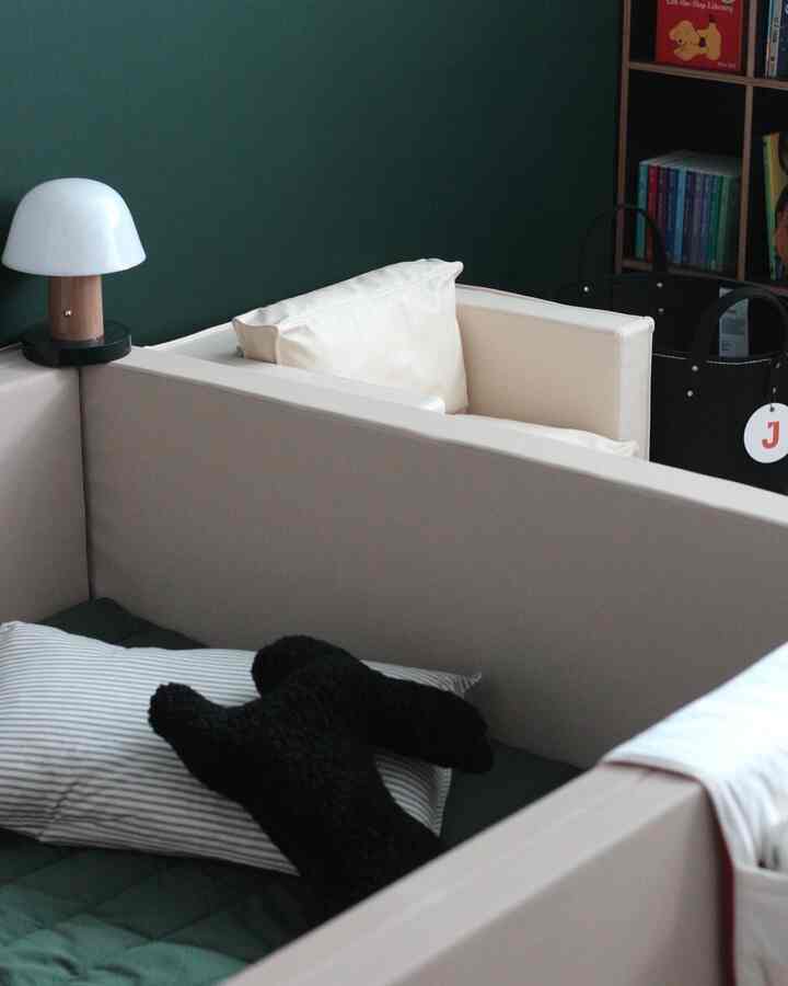 濃い緑色の壁とベージュ色のベビー用バンパーベッドが配置された子供部屋のインテリア