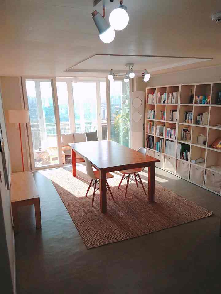 Bright natural-toned living room featuring a dining table and bookshelf with cozy atmosphere and abundant natural light through large windows