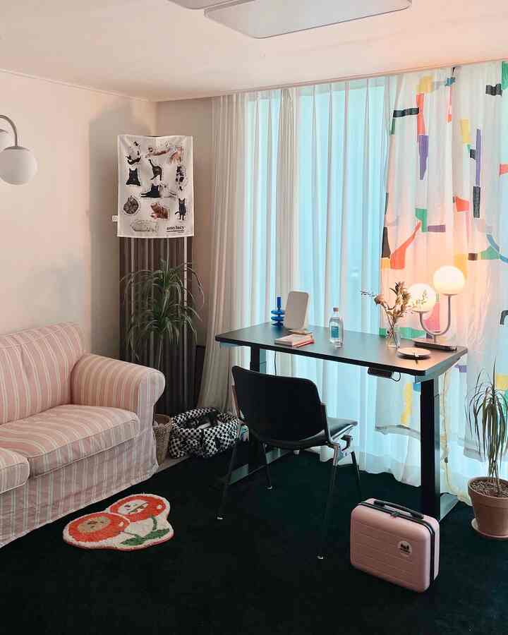 Bright white and pink-toned living room featuring a two-seater sofa and black desk creating a cozy home office