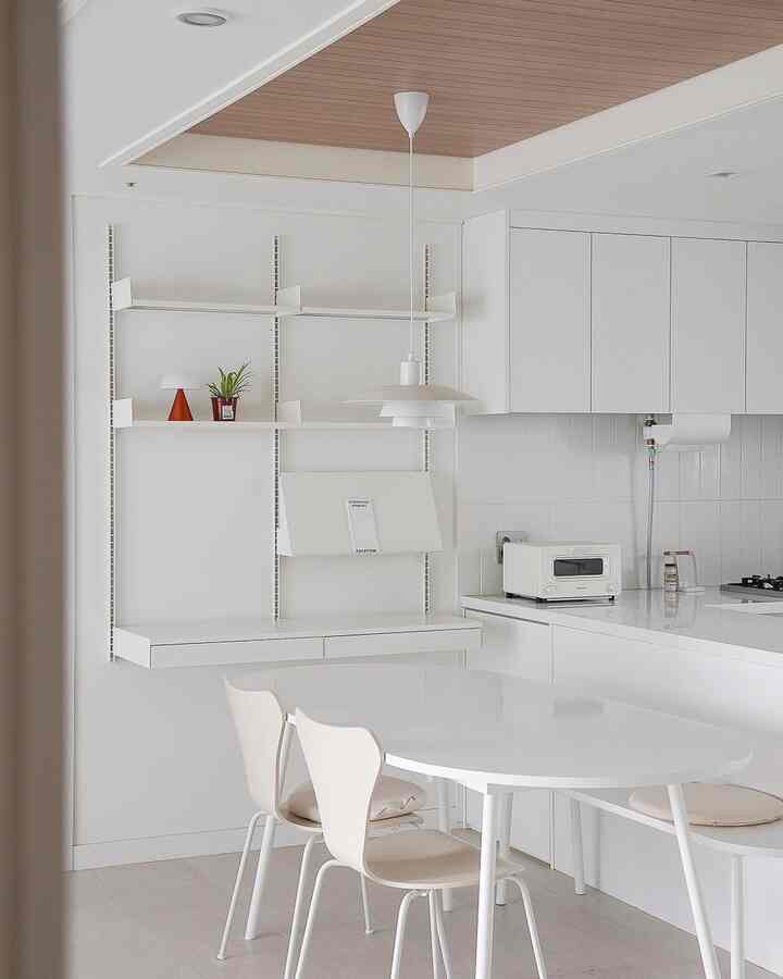 白と木目調の調和のとれたキッチン、壁棚とダイニングテーブルが配置されたシンプルで清潔感のあるインテリア