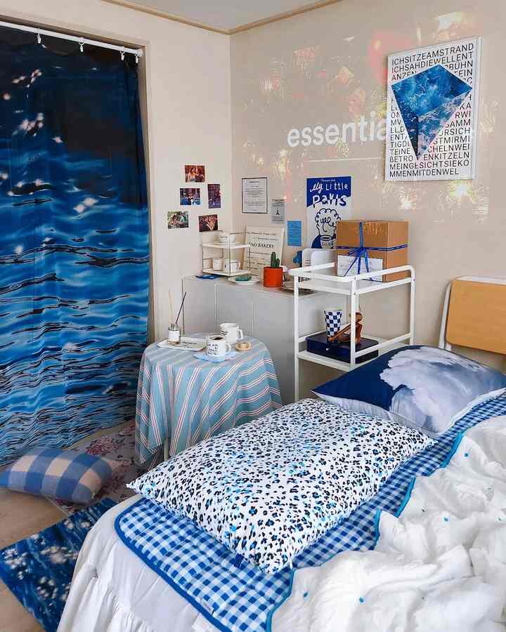 Blue and white toned compact bedroom featuring a bed with patterned pillows, small table, and shelving creating a cozy atmosphere