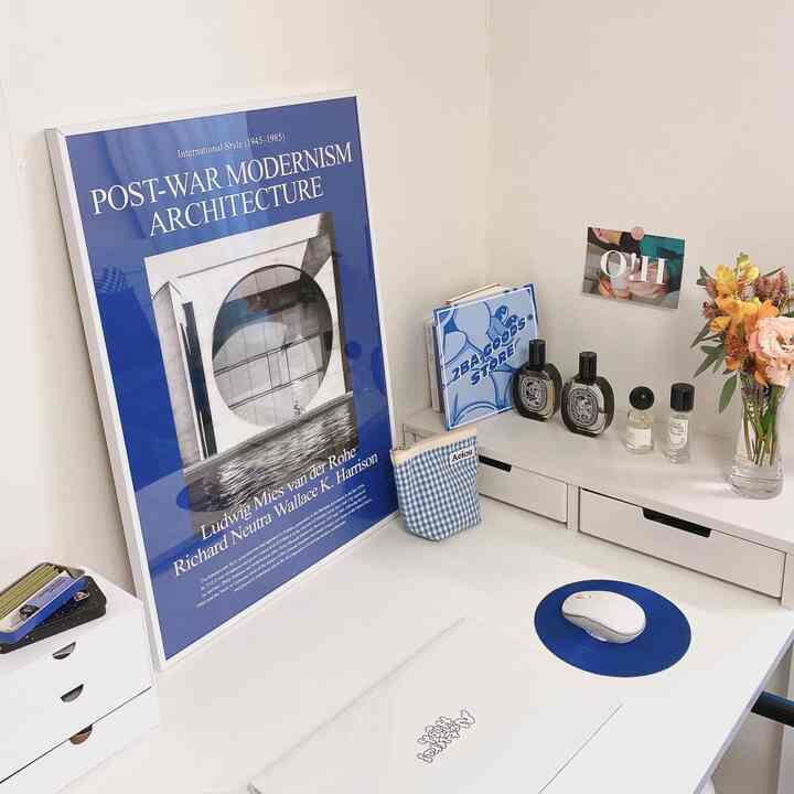 White and blue toned home office featuring a desk with a modernist poster, vase, and organized minimalistic elements