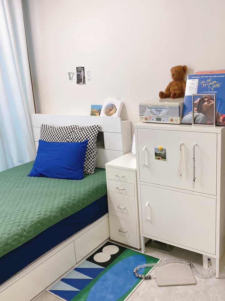 A cozy bedroom with white, blue, and green tones featuring modern furniture and a geometric patterned rug in a compact space