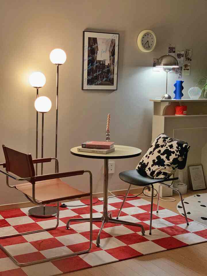 A living room with red and white checkerboard rug featuring a round table and Mid-Century Modern chairs, creating a cozy home cafe atmosphere