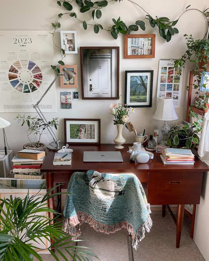 ナチュラルな色調のホームオフィス、木製デスクにカレンダーや額縁、植物、ブランケットが配置された雰囲気のある作業空間