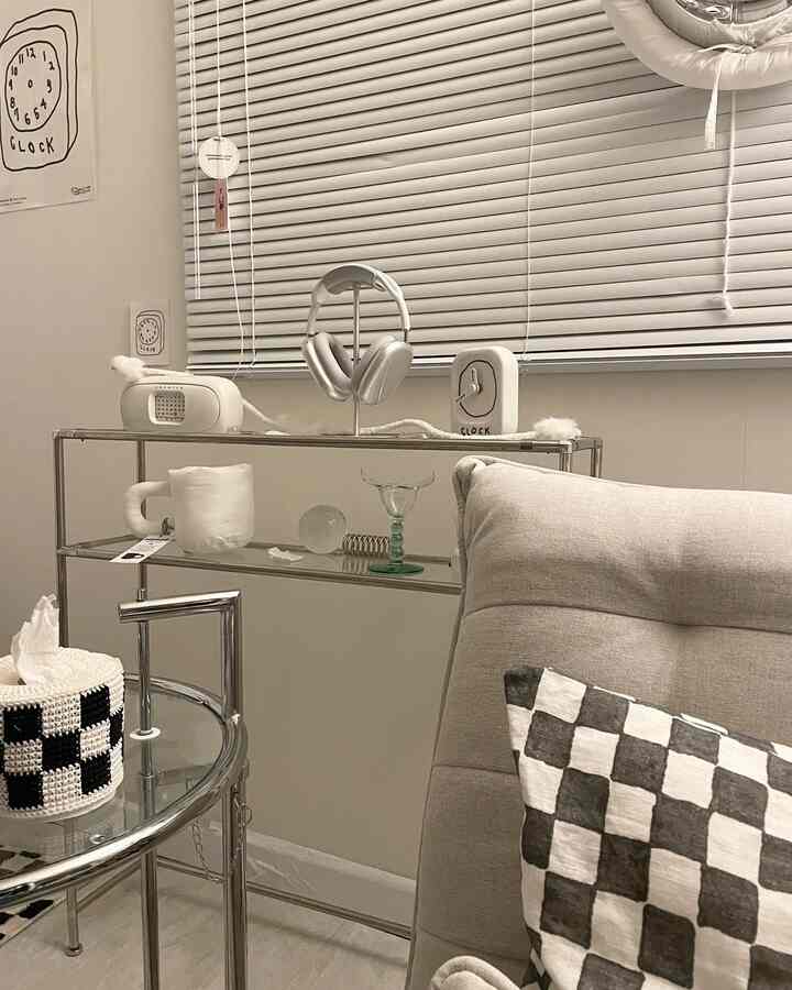 A white and gray toned living room featuring aluminum blinds, metal console table, sofa bed, and checkered cushion in a simple setting