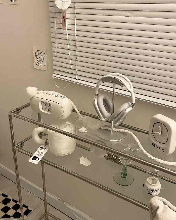 White-toned small room featuring aluminum blinds, stainless steel console, and AirPods Max in a modern setting