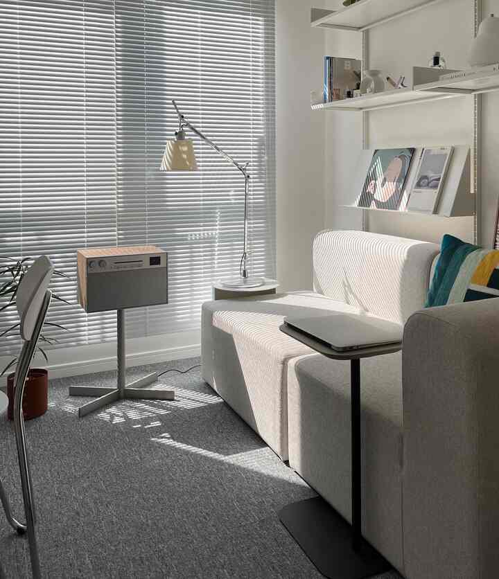 Modern living room in white and gray tones featuring sofa, blinds, and side table with a simple atmosphere