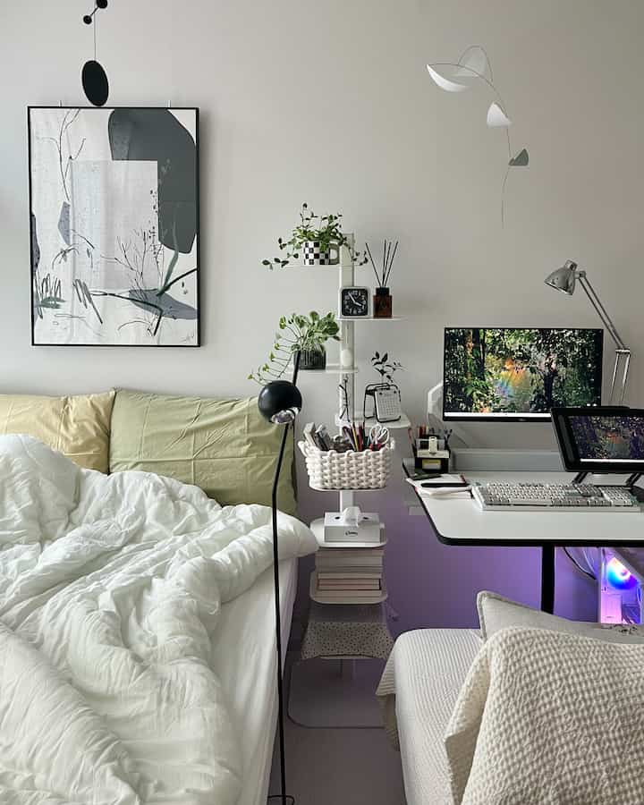 White and green toned studio apartment home office featuring bed, desk, plants, and framed art with a clean, cozy atmosphere