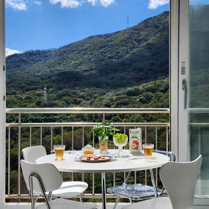 白を基調としたバルコニーダイニング、丸テーブルと椅子が配置され、自然の丘陵風景を望める空間