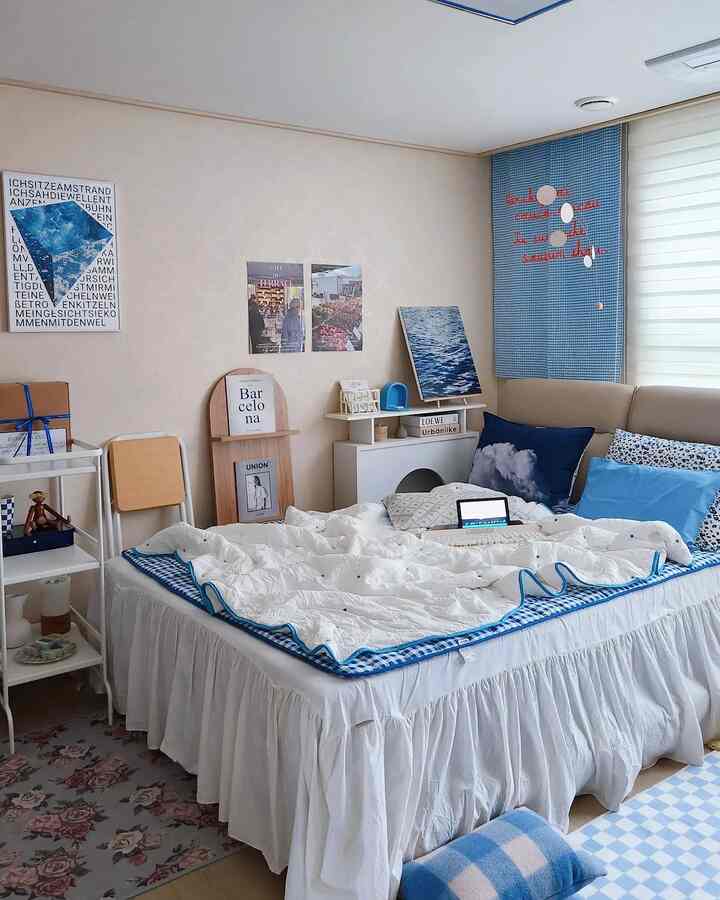 白と青の色調の寝室、ベッドとクッション、ポスターが配置された雰囲気のあるレトロな空間