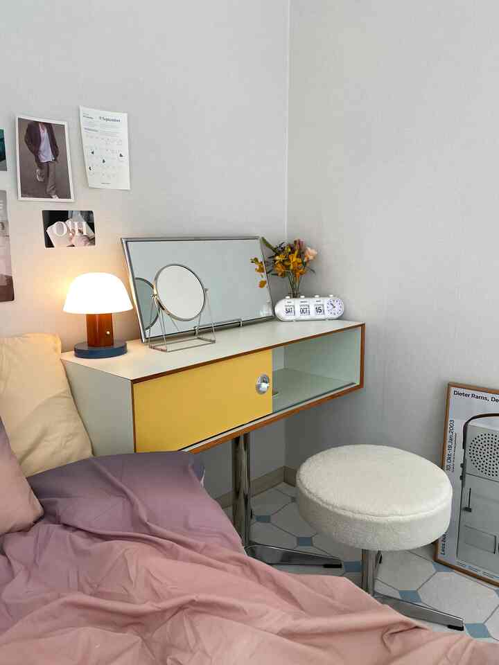 A compact single-room makeup space with pink and yellow accents, featuring a console vanity and a white stool in a natural tone setting