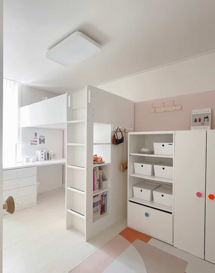 A white and pink toned kids' room featuring a loft bed, desk, and multifunctional storage creating a cozy atmosphere