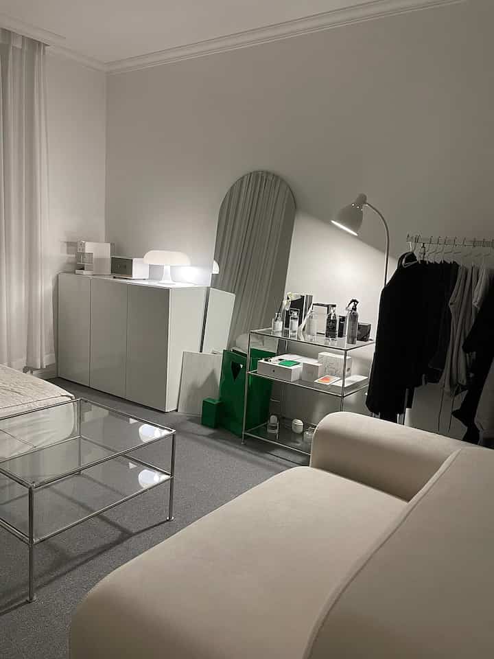 White and gray toned living room featuring large sofa, metal frame side table, full-length mirror, and floor lamp with a clean minimal atmosphere