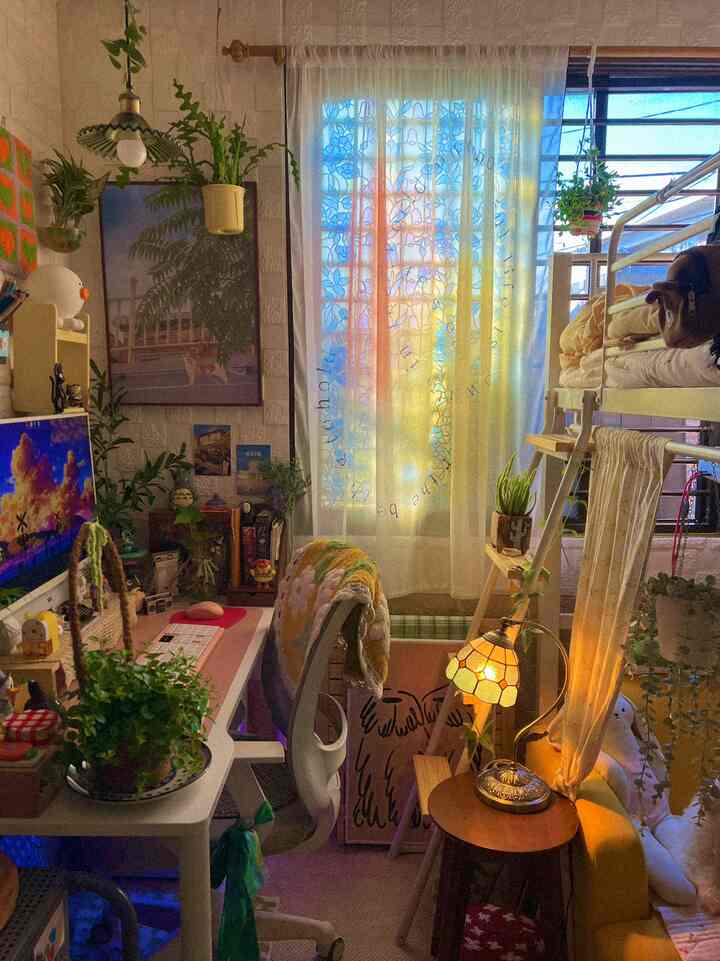 暖かな日差しと透けるシフォンカーテンが印象的なワンルーム型の感性あふれるホームオフィス空間、植物とヴィンテージ照明で彩られた居心地の良いインテリア