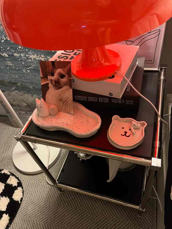 鮮やかな赤いテーブルランプと黒いサイドボードに猫の写真と陶器のオブジェが配置されたインテリア空間