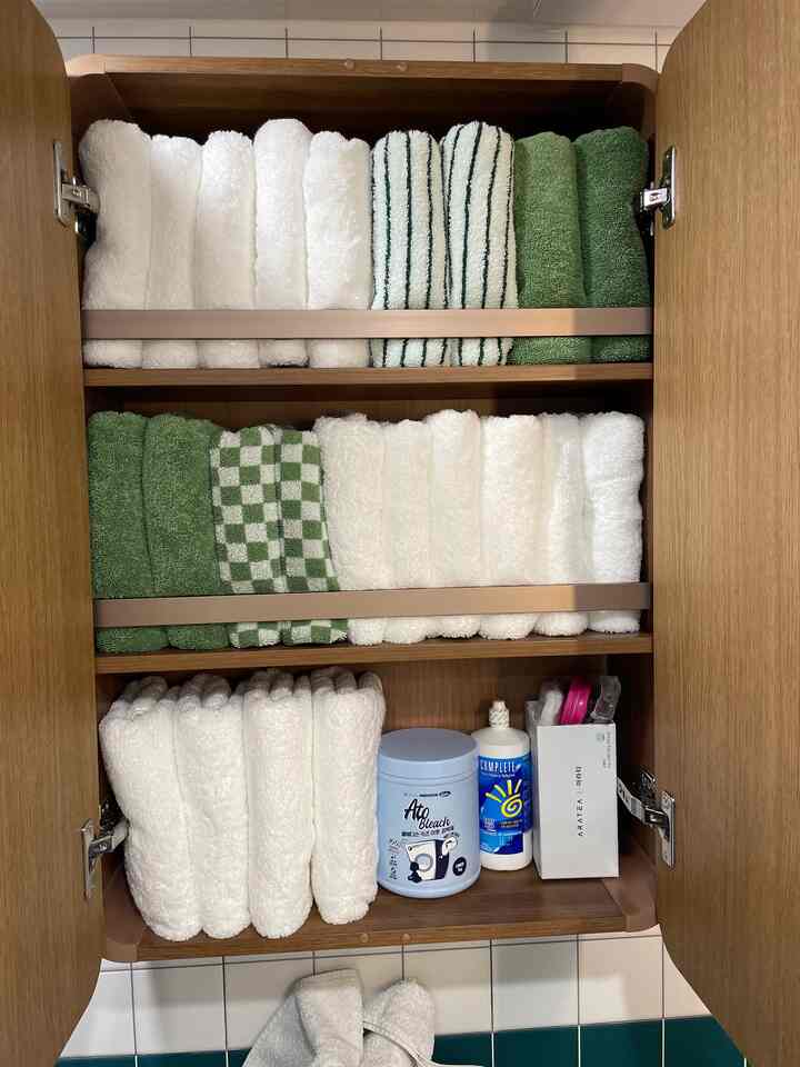 白と緑のタオルが整然と並べられた浴室の木製棚