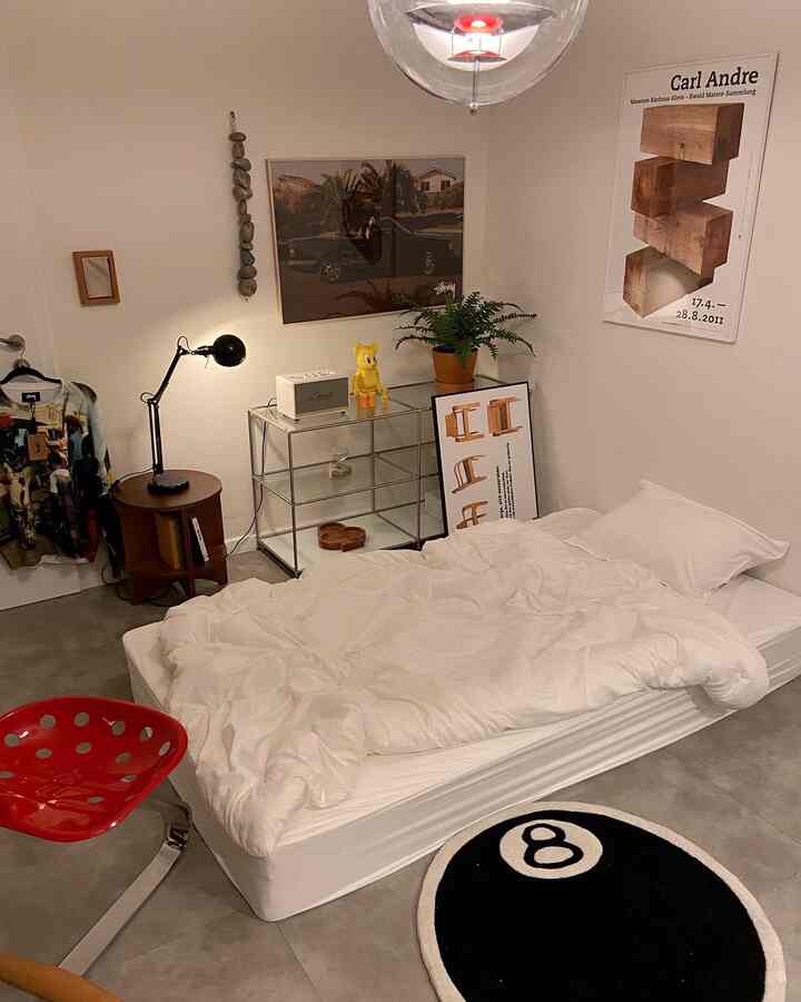 白と黒のトーンのワンルーム寝室、シンプルな寝具と木製ナイトテーブル、植物と壁アートが調和したモダンなインテリア