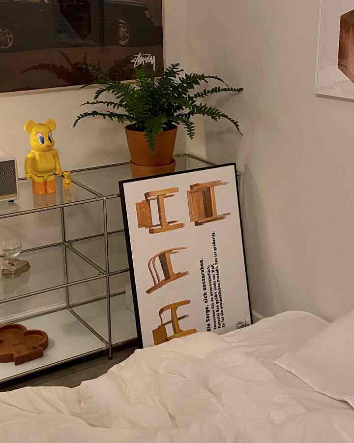 ホワイトとナチュラルブラウン調のミニマルな寝室、ベッドとモジュール収納棚、植物と額入りアートが配された空間