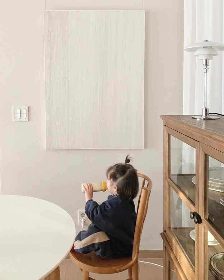 White and wood-tone dining room with a child sitting on a chair drinking from a bottle, creating a peaceful atmosphere