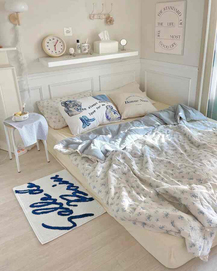 Bright white-tone bedroom featuring a low-profile bed with soft bedding and a floor lamp, cozy cottage style space