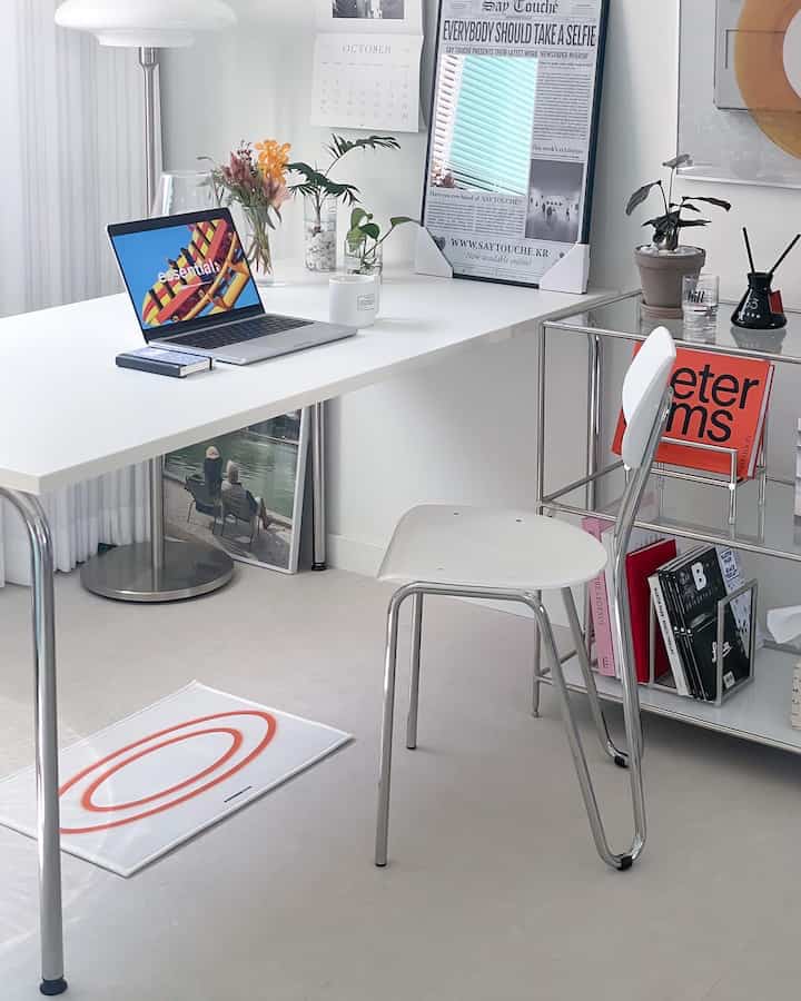 White and silver toned home office space featuring a simple modern desk, chair, and plants with clean interior design