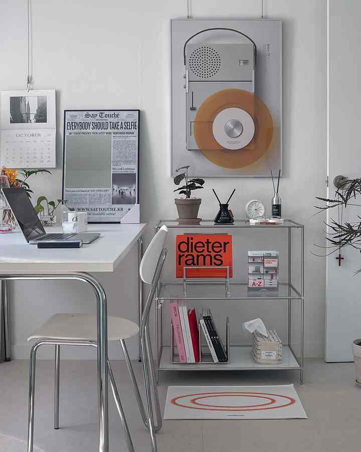 White and silver-toned home office featuring a desk, chair, bookshelf, and picture frames with a clean interior ambiance