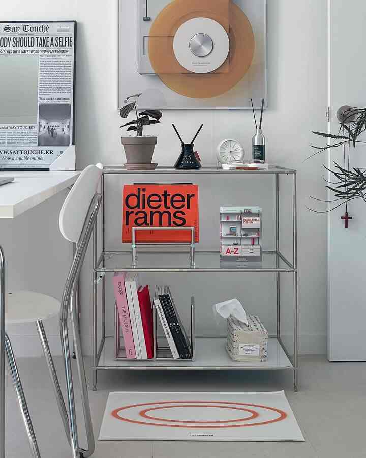Modern living room with white tones, featuring a steel shelving unit, books, and minimal interior objects arranged neatly