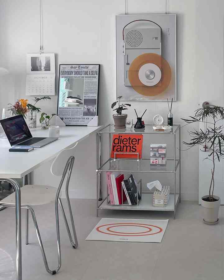 White and gray toned home office featuring a clean desk, shelving with books and plants, and a simple workspace