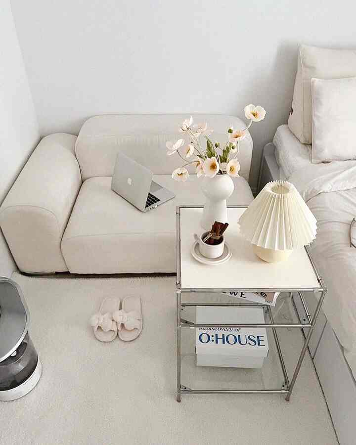 White and beige toned bedroom featuring a simple sofa and bed, cafe-style vase and lamp creating a cozy atmosphere
